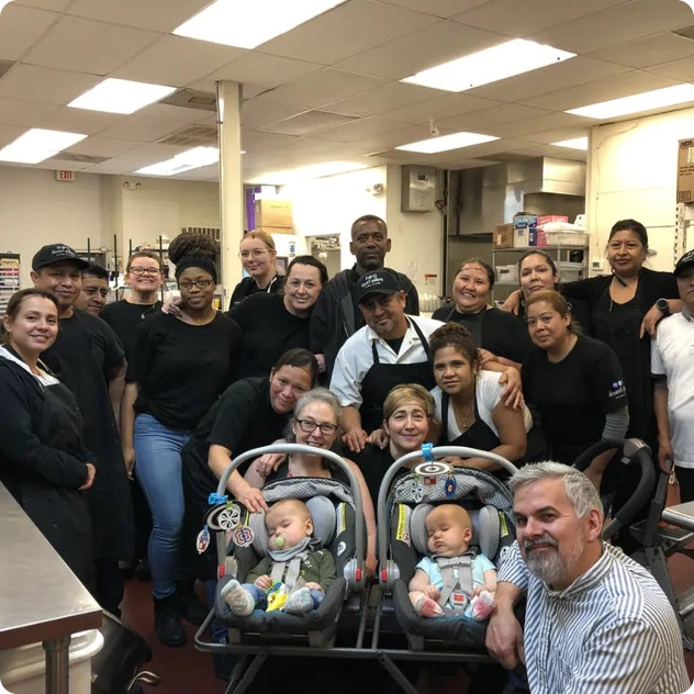 Large group of restaurant staff posing with two infants in carriers.