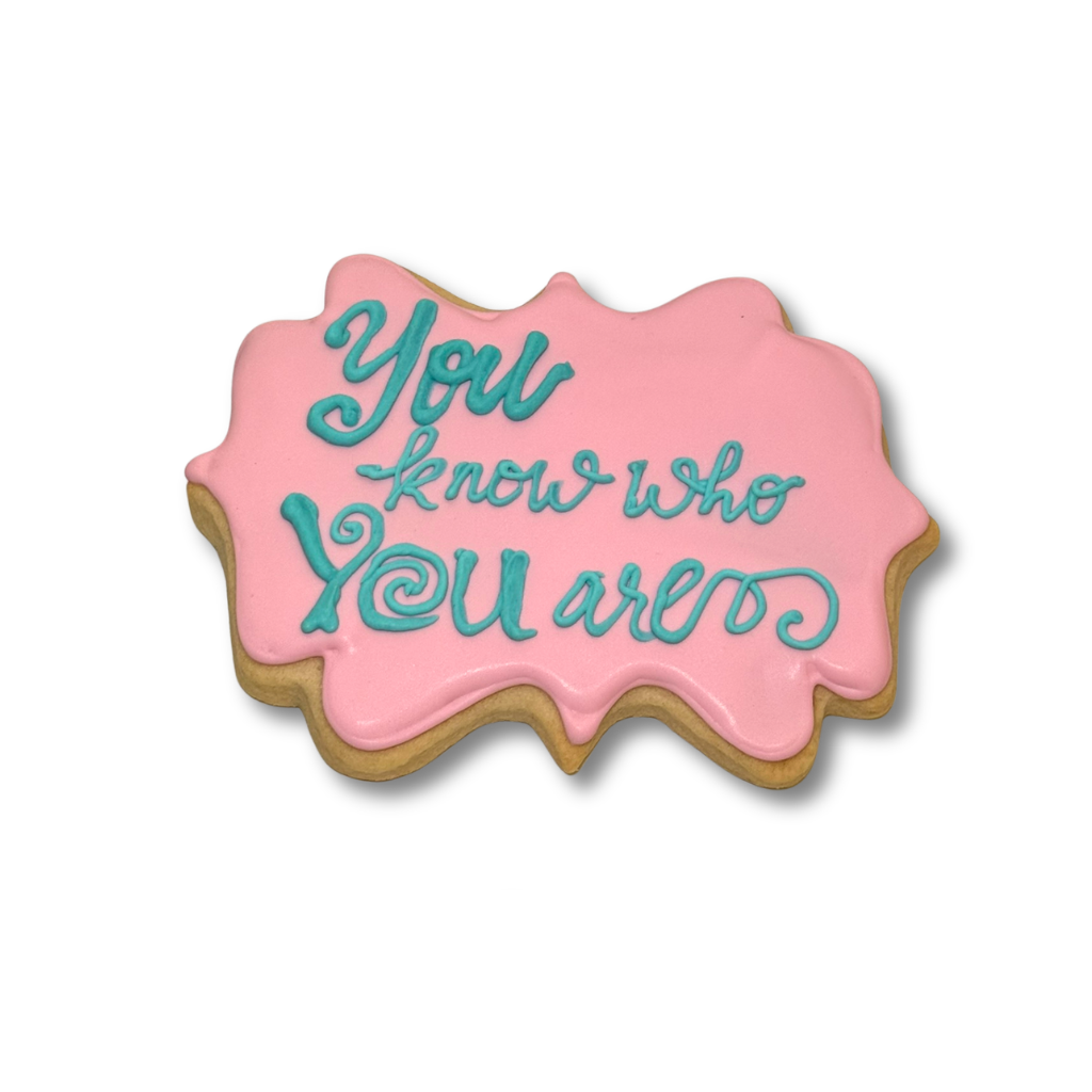 Moana cookie with pink icing and teal cursive lettering.