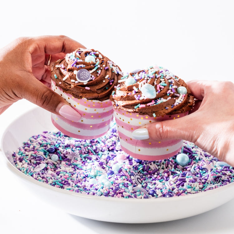 Two chocolate cupcakes in pink striped liners with sprinkles.