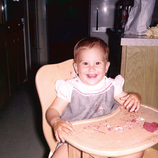 Smiling baby in a high chair with food on their face and hands