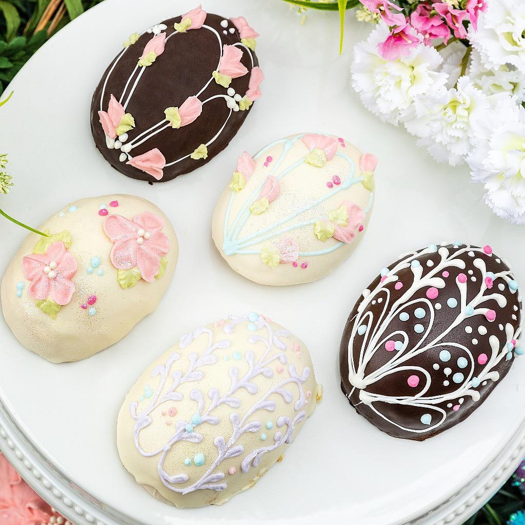 Five chocolate Easter eggs decorated with floral icing on a plate.