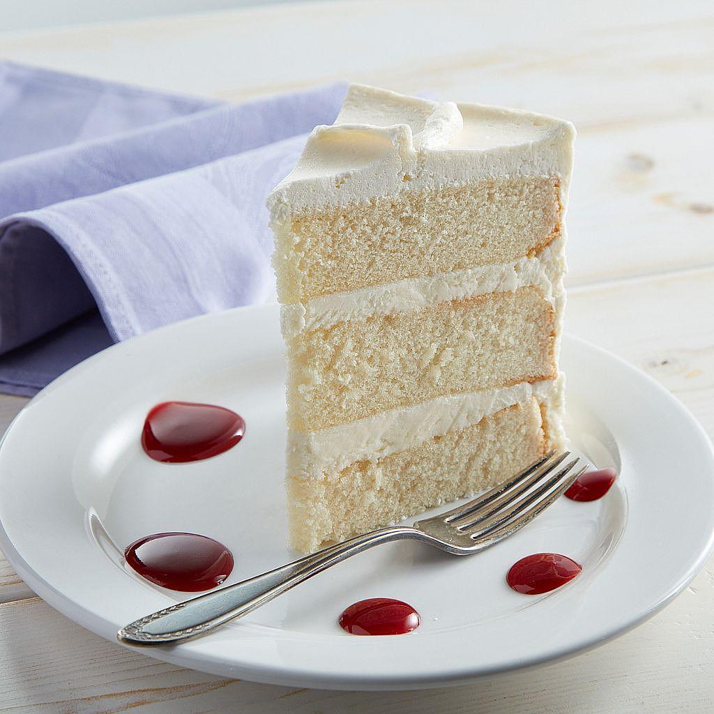 Slice of white layer cake with berry sauce on a plate