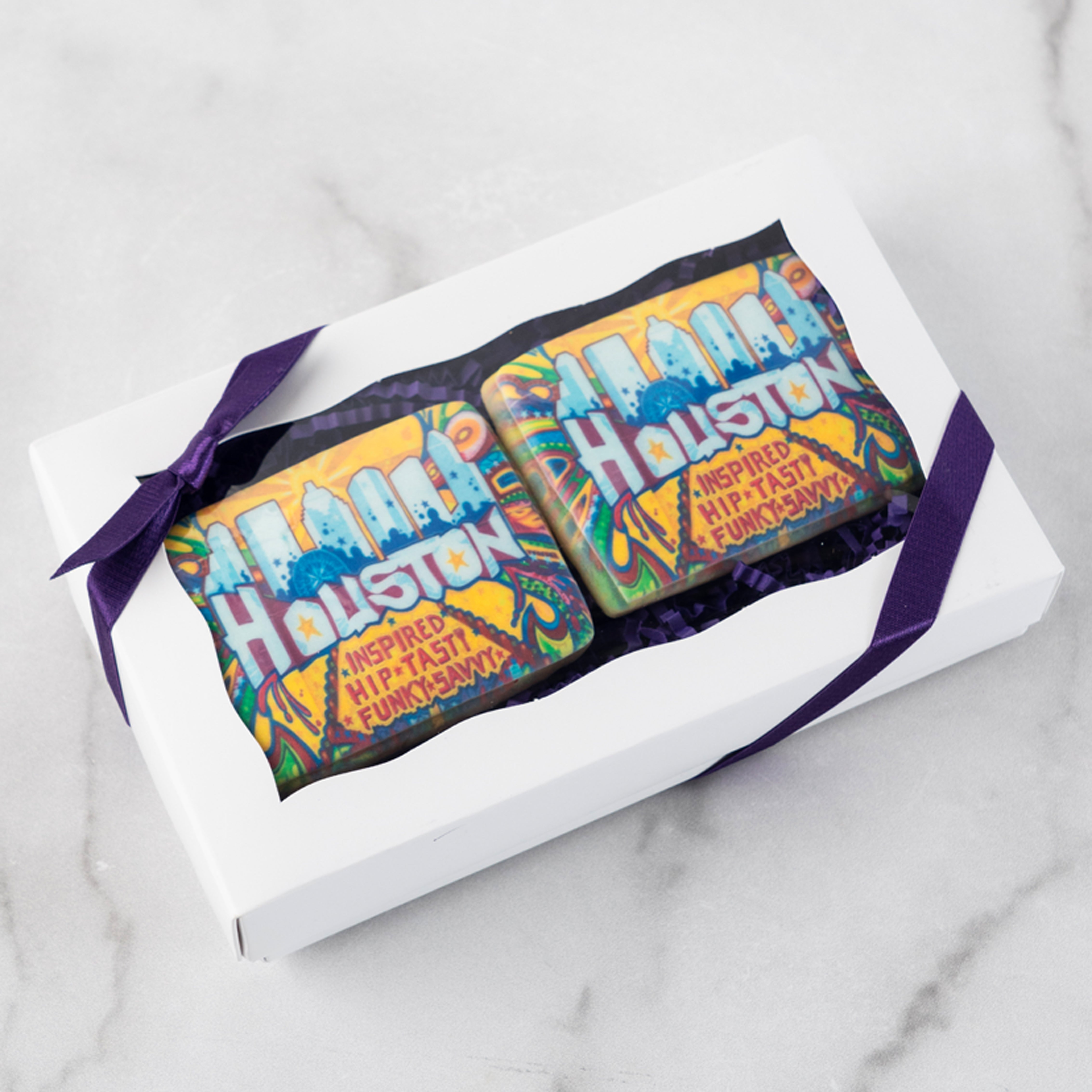 Two Houston-themed logo cookies in a white gift box with purple ribbon.