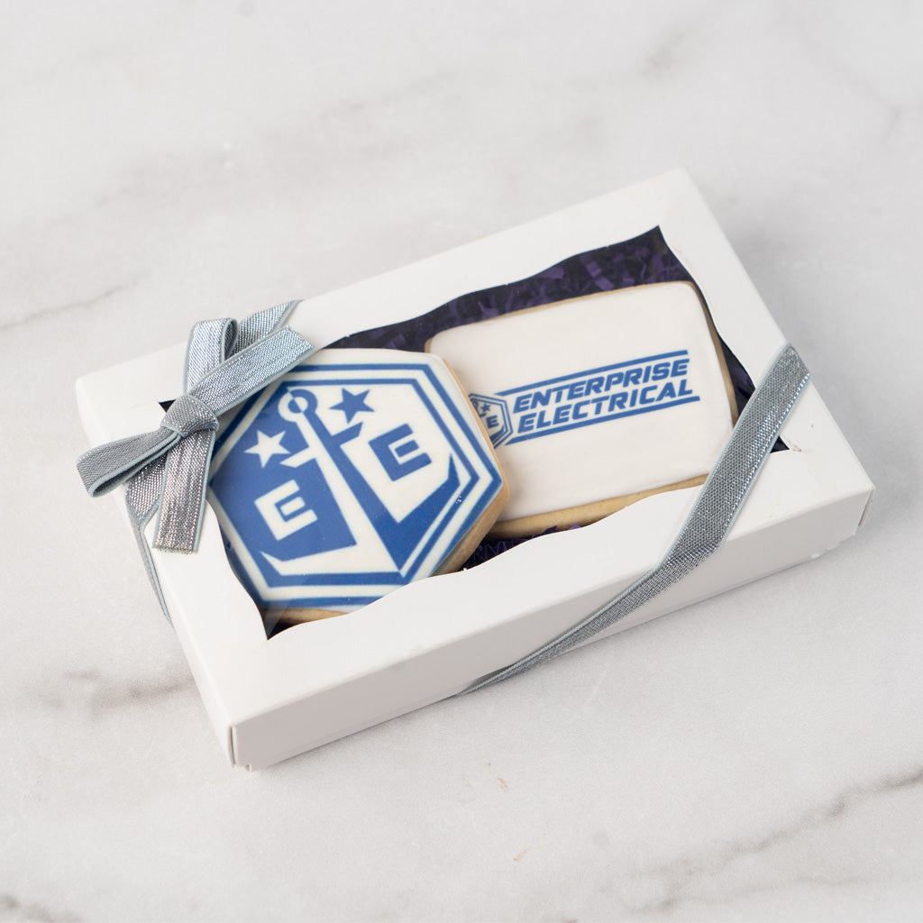 Two custom logo cookies in a white gift box with silver ribbon.