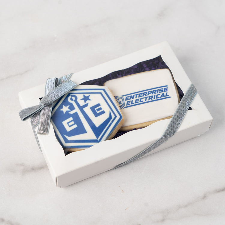 Two custom logo cookies in a white gift box with silver ribbon.
