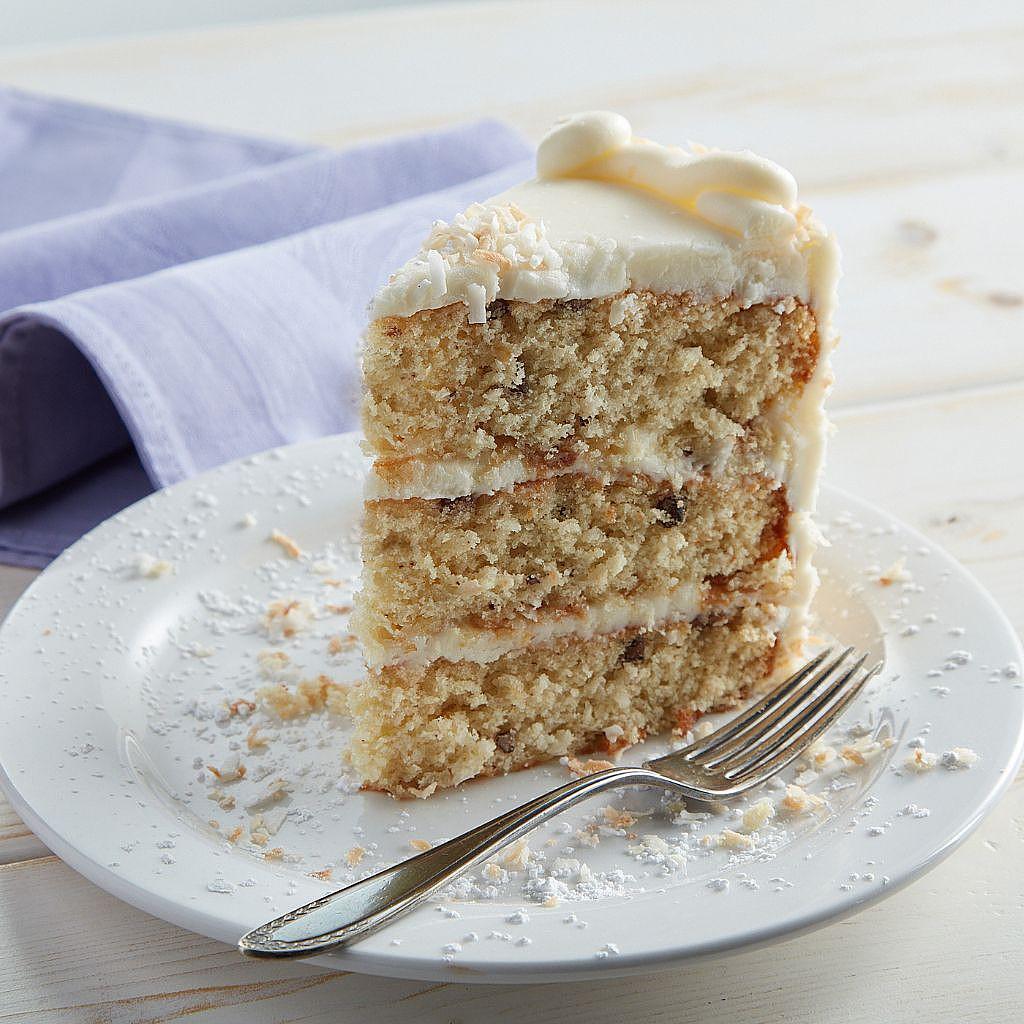 Slice of coconut layer cake with frosting on a white plate