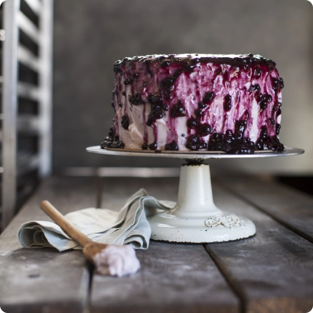 Blueberry cake with dripping fruit glaze on a cake stand