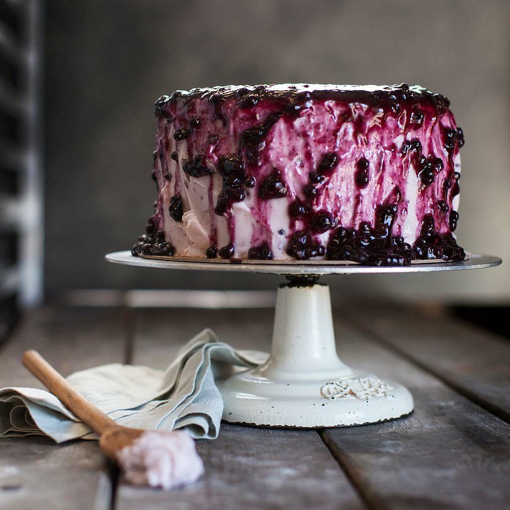 9-inch lemon blueberry cake with a thick berry glaze on a stand.