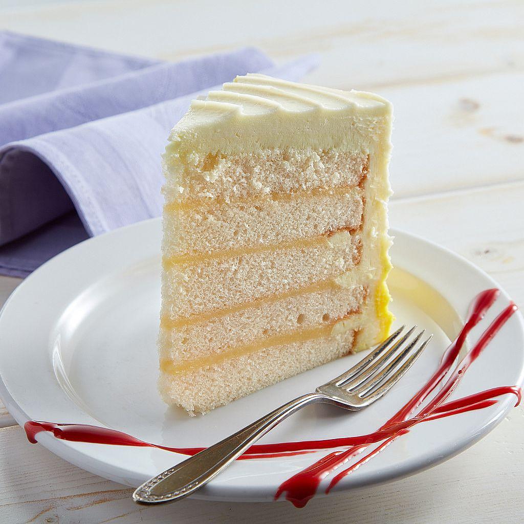 Luscious Lemon Cake slice with yellow layers on a white plate.