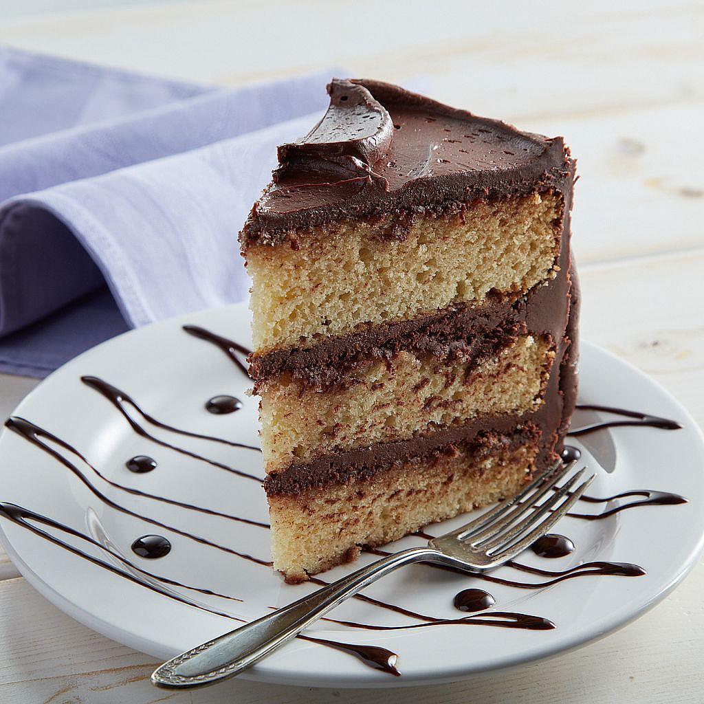 Slice of yellow cake with chocolate frosting on a plate