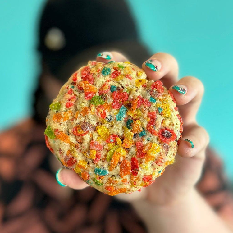 Fruity Pebbles cookie held in hand against a blue background.