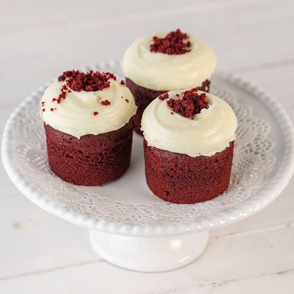 Red velvet cupcakes with cream cheese frosting on a white stand.