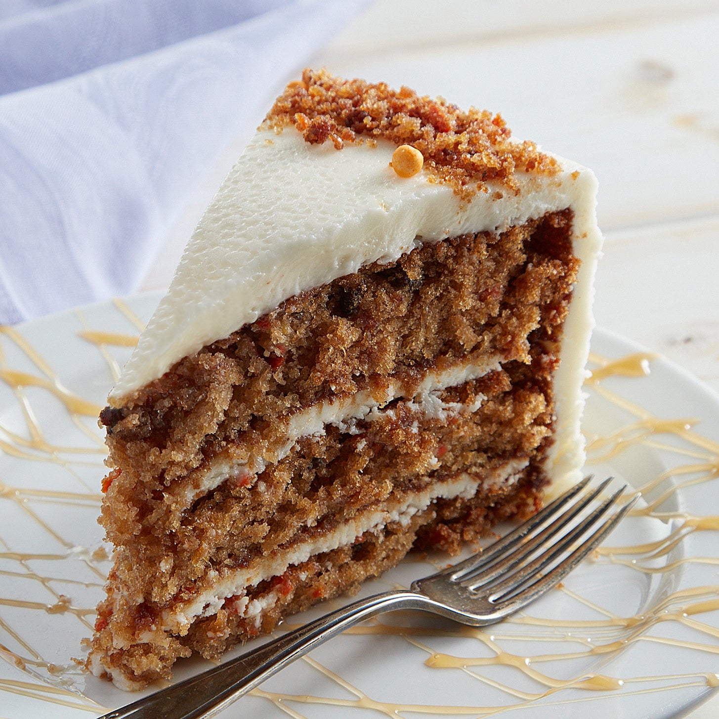 Carrot cake slice with cream cheese frosting on a drizzled plate.