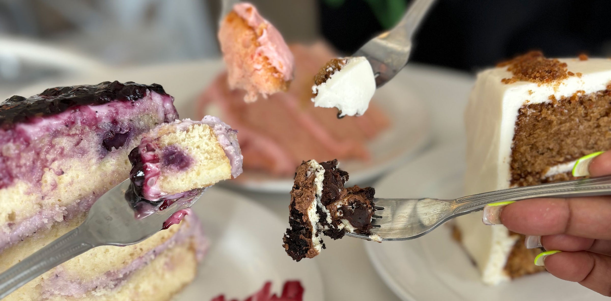 Forks holding bites of blueberry, chocolate, and pink cakes