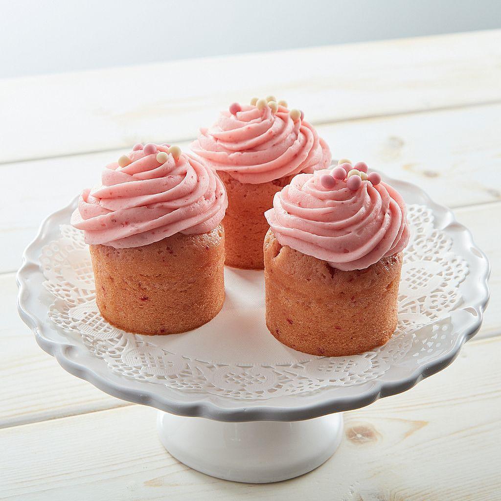 Three strawberry cupcakes with pink frosting on a white stand.
