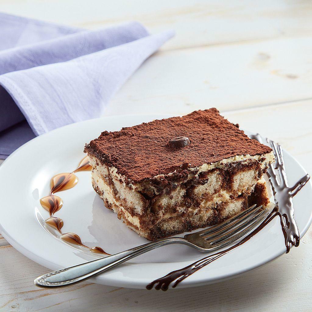 Tiramisu slice on a white plate with a fork and cocoa dusting.