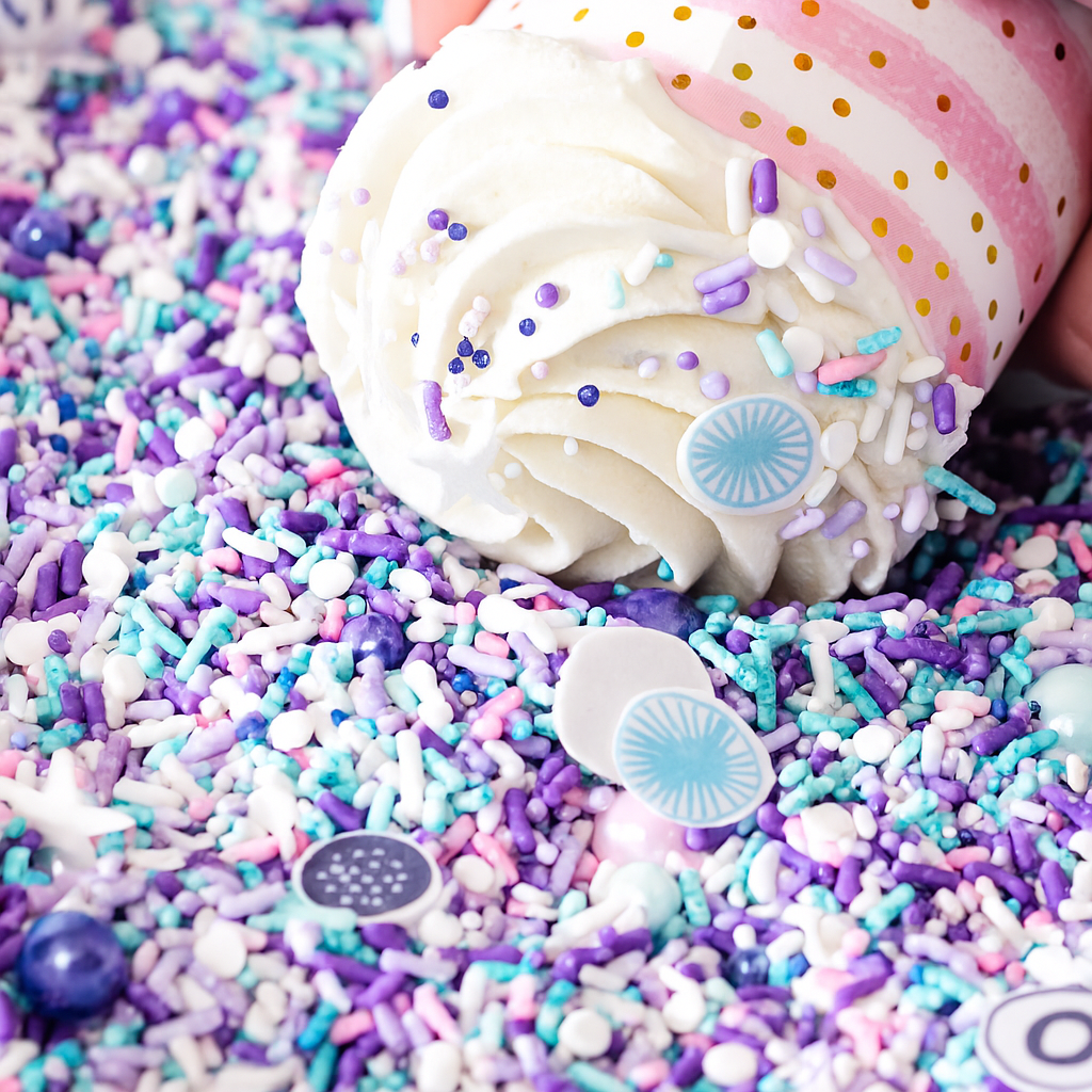 Vanilla cupcake with white frosting on purple and blue sprinkles.